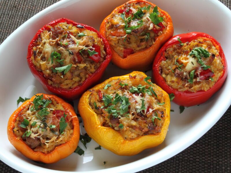 Enjoy a delightful stuffed peppers recipe featuring five colorful bell peppers filled with a savory meatball mixture, topped with melted cheese and chopped parsley, all beautifully presented in a white oval baking dish. _MamaMancinis