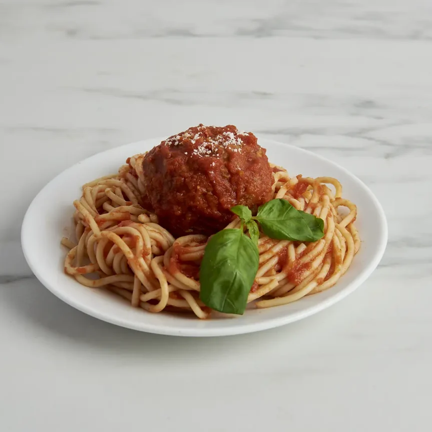 A plate of spaghetti topped with Costco's Italian Style Sauce and a jumbo beef meatball, garnished with fresh basil, on a marble surface. _MamaMancinis