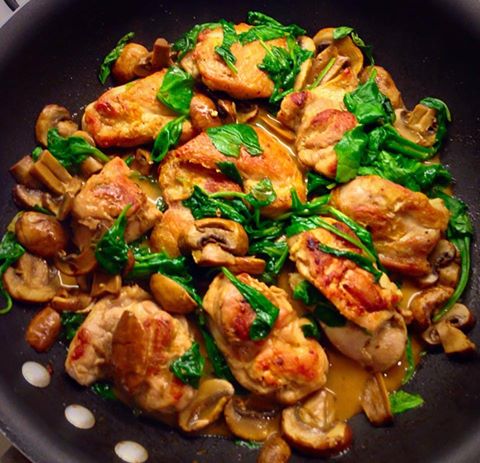 A skillet filled with perfectly browned chicken thighs is glazed and mixed with fresh spinach leaves and sliced mushrooms. These ingredients are beautifully distributed in a savory sauce, making each bite a harmonious blend of flavors. _MamaMancinis