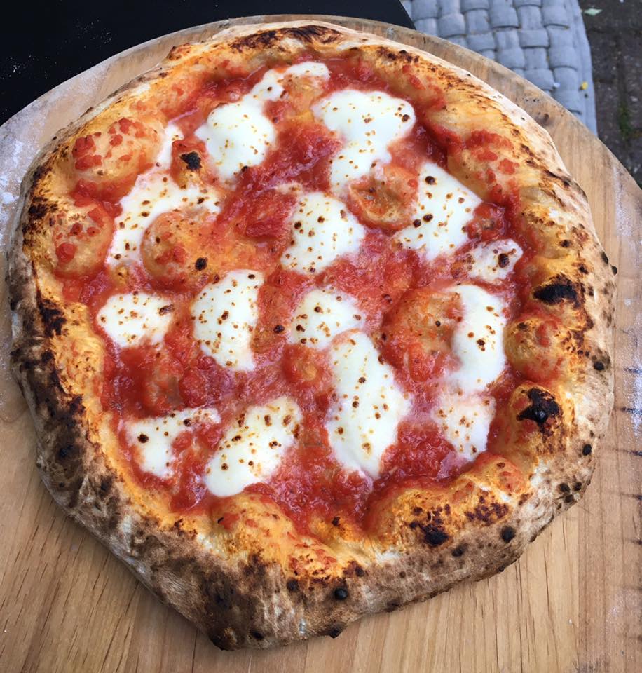 A delicious Neapolitan pizza with a bubbly, charred crust, crafted from freshly kneaded dough, topped with melted mozzarella cheese and vibrant red tomato sauce on a wooden board. _MamaMancinis