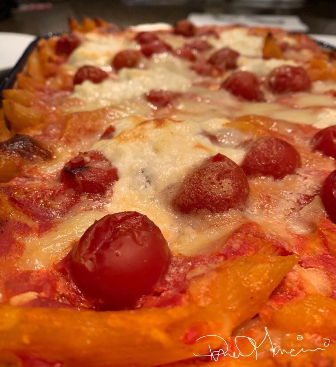 A close-up of Meatball Baked Ziti with melted cheese, cherry tomatoes, and tomato sauce, showing a golden, bubbly surface and perfectly browned edges. _MamaMancinis